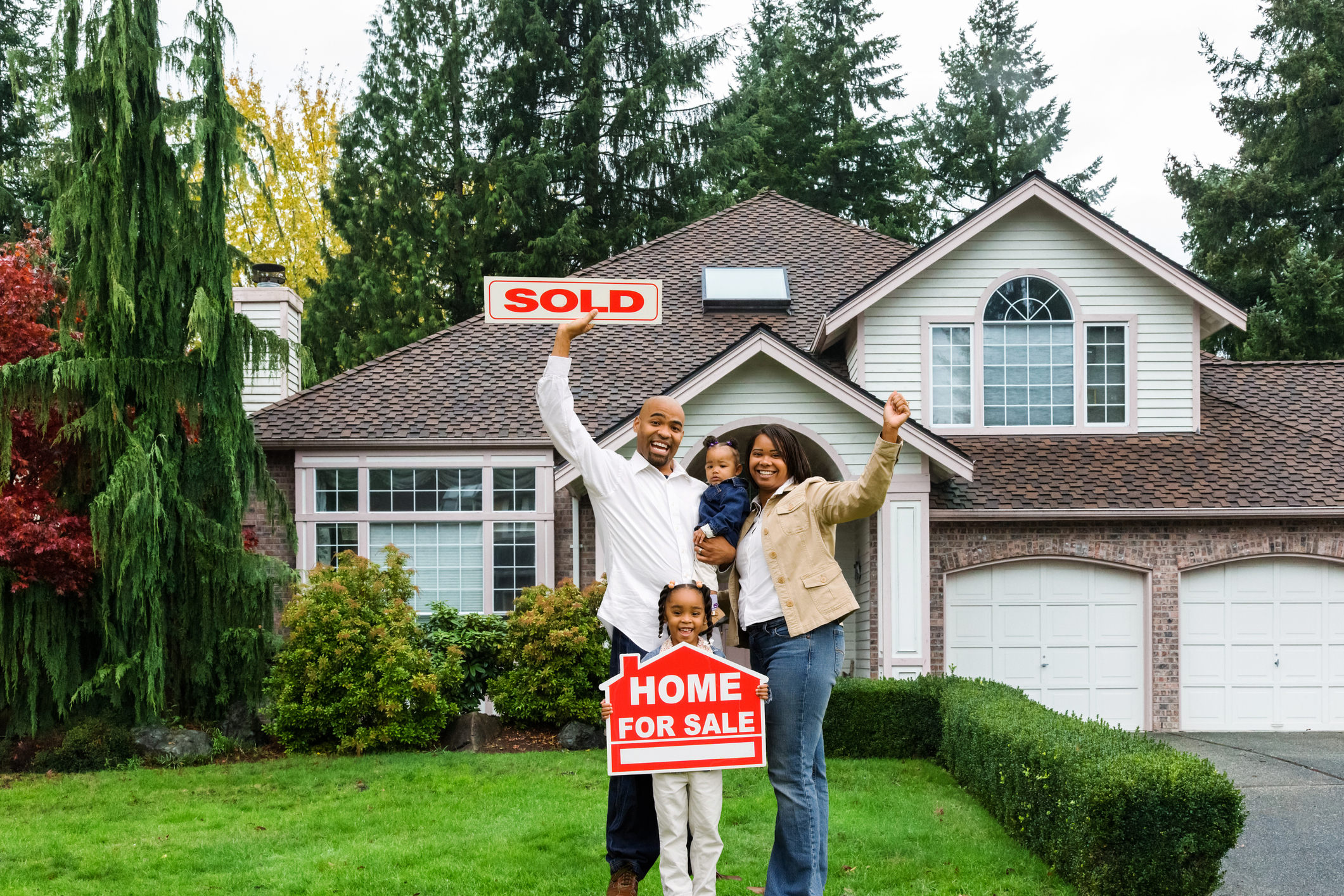 Family of four poses in front of their house with the sold sign held in the air 