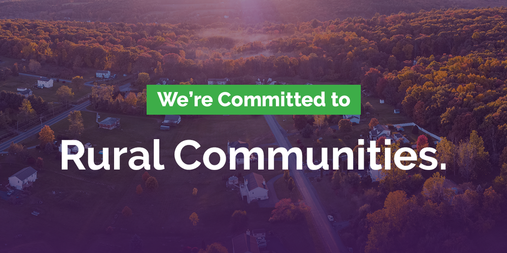 Rural countryside featuring rolling hills and trees with text reading: We're Committed to Rural Communities.